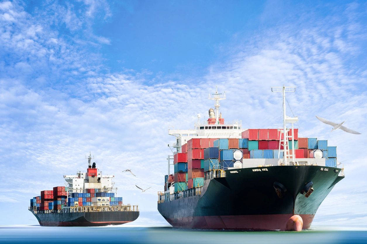 Two large cargo ships in the ocean under a blue sky.